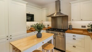 A modern kitchen with white cabinetry, a stainless steel range hood, a Bosch microwave, and a wooden island with stools.