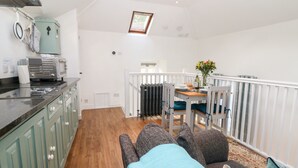 A compact kitchen with modern appliances, a dining area with a table set for two, and a cozy seating area with a view of the outdoors. - The Bath House (Moreton-in-Marsh)
