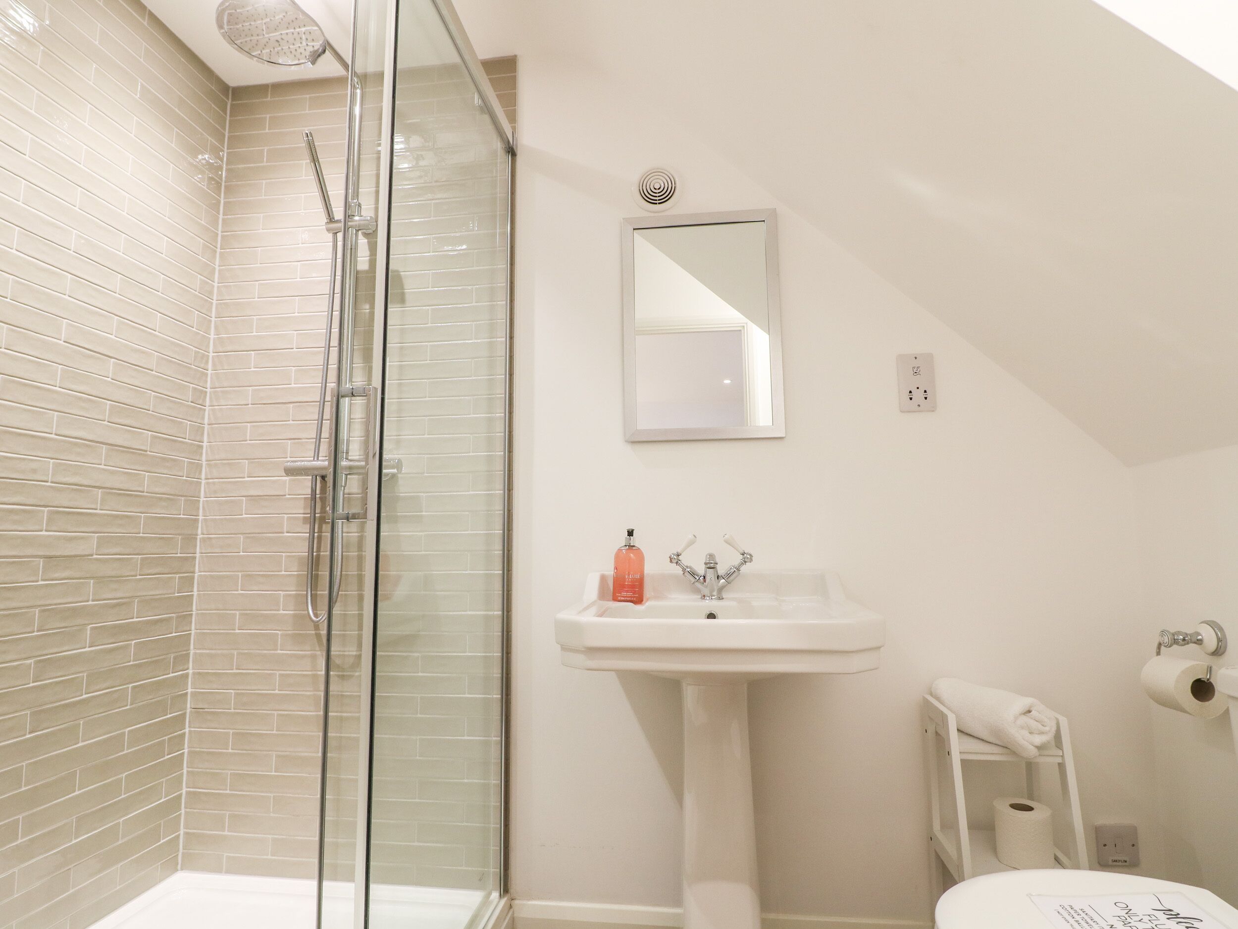 A bathroom with a glass shower enclosure, a white sink, a mirror, and a toilet.