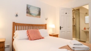 A neatly made bed with a wooden headboard, a single decorative pillow, and a bedside lamp. - The Bath House (Moreton-in-Marsh)