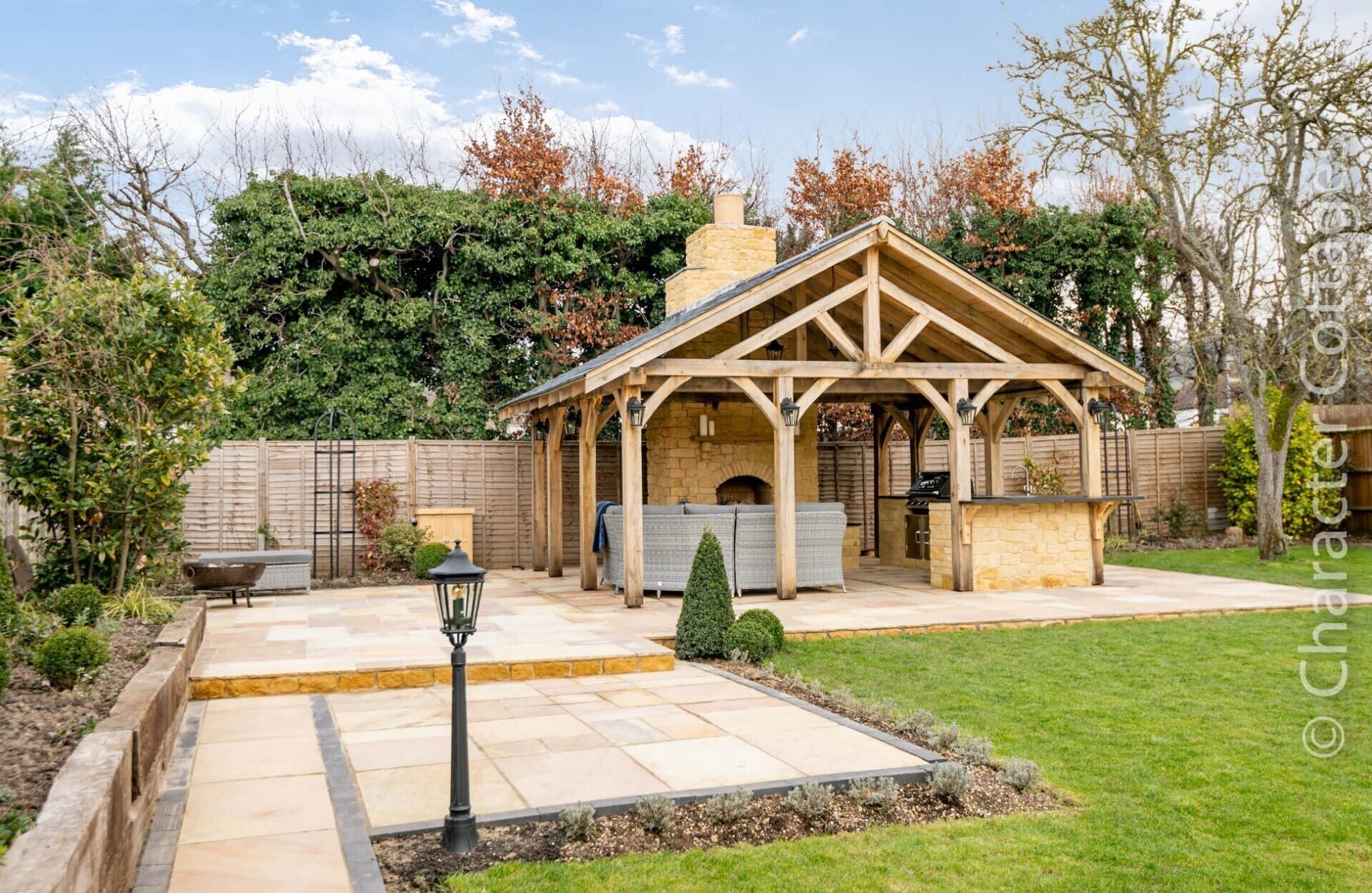 A covered patio area with a stone fireplace, seating, and a barbecue grill.