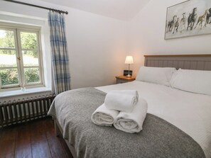 A hotel room with a large bed, a nightstand with a lamp, a window with curtains, and a painting on the wall.