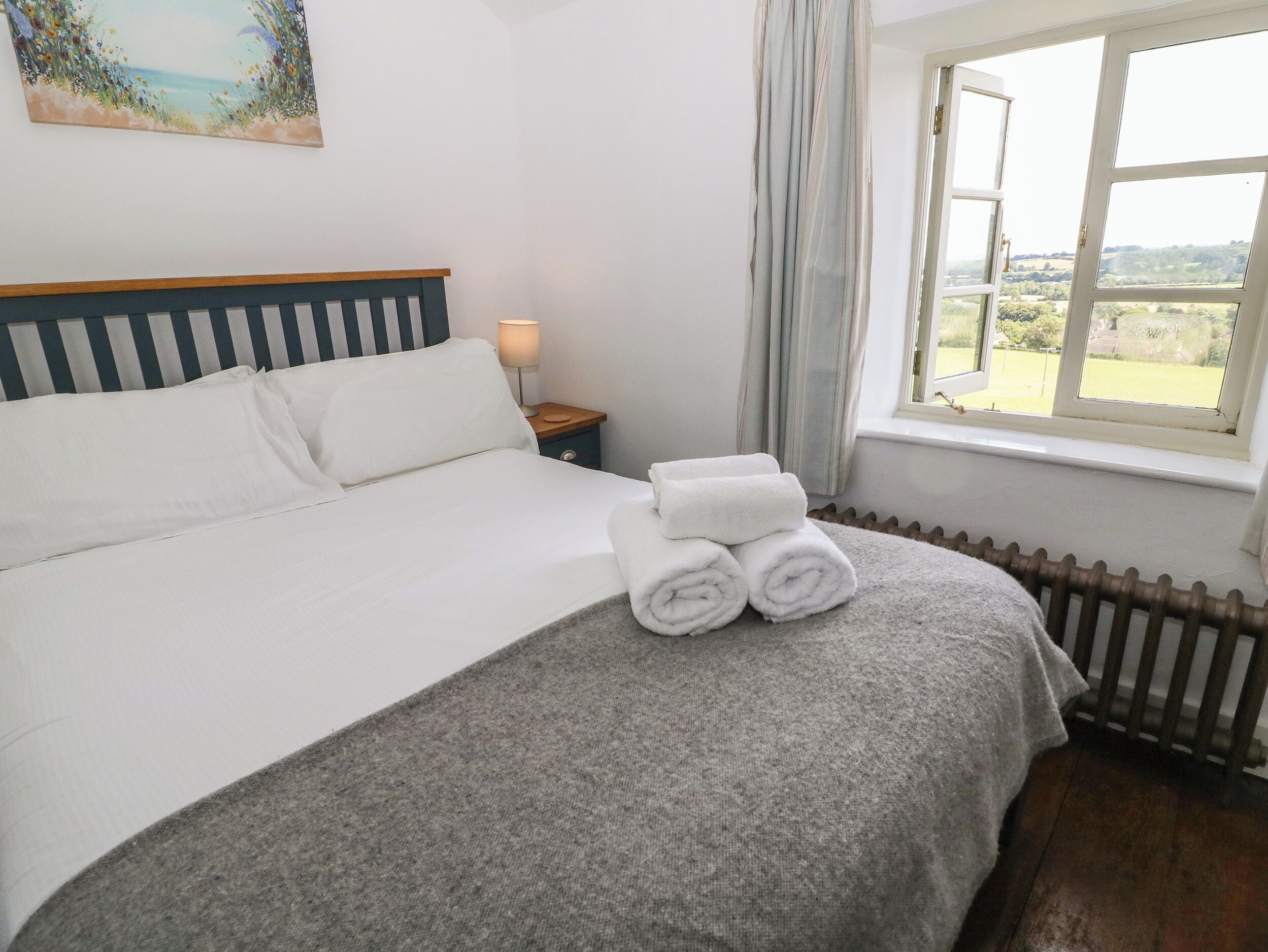 A neatly made bed with white linens, a bedside lamp, and a view of a green landscape through a window.