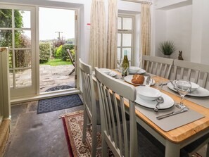 A dining area with a table set for two, a window with curtains, and a view of the garden outside.
