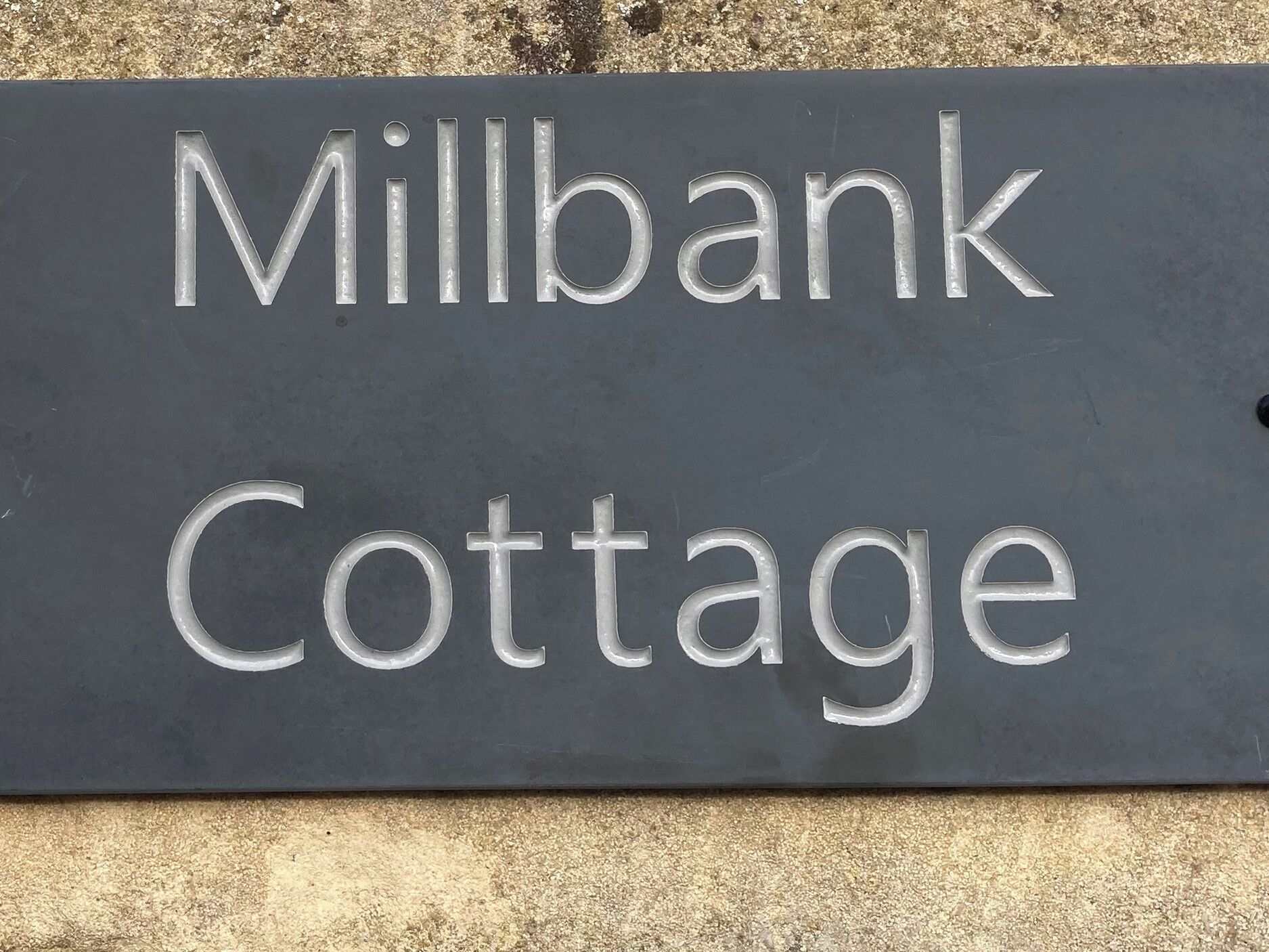 A sign with the text "Millbank Cottage" on a dark background.
