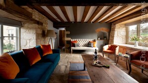 Un salon rustique avec des poutres apparentes, un canapé bleu agrémenté de coussins orange, une table basse en bois et une cheminée en pierre.