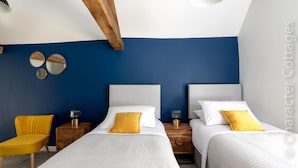A bedroom with two beds, a yellow chair, and wooden nightstands. - The Creamery (Stonehouse)