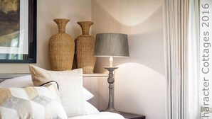 Une chambre à coucher avec un lit, deux vases en osier, une lampe et un tableau au mur.