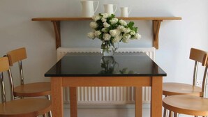 A dining table with a vase of flowers, two chairs, and a shelf with three white pitchers.