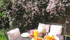 A breakfast setup with croissants, a bowl of fruit, a jug of orange juice, and honey on a metal table outdoors.