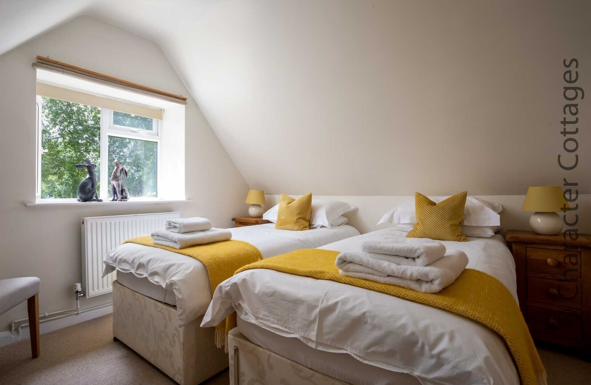 A bedroom with two beds, a window with a view of trees, and a radiator.