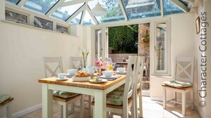 Une véranda avec une table à manger en bois, mise pour le petit-déjeuner, des chaises blanches et une vue sur le jardin.