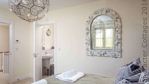 A bedroom with a bed, a large mirror, a chandelier, and a view of the bathroom. - Honeystones (Cheltenham)