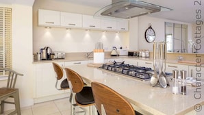 A modern kitchen with a central island, stainless steel appliances, and wooden chairs. - Honeystones (Cheltenham)