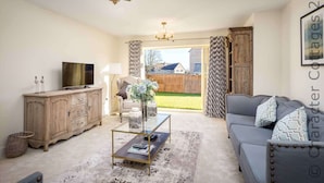 A living room with a television, wooden cabinet, glass coffee table, and grey sofa. - Honeystones (Cheltenham)