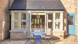 A cottage with a stone exterior, a tiled patio, and a blue table with chairs. - Honeystones (Cheltenham)