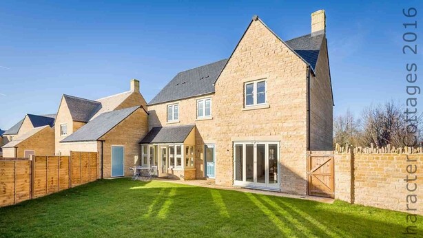 A large, two-story house with a well-maintained lawn, a wooden fence, and a stone wall. - Honeystones (Cheltenham)