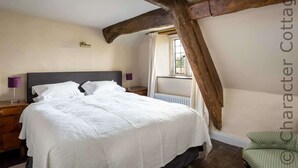 Een slaapkamer met een groot bed, houten balken, een raam en een groene stoel.