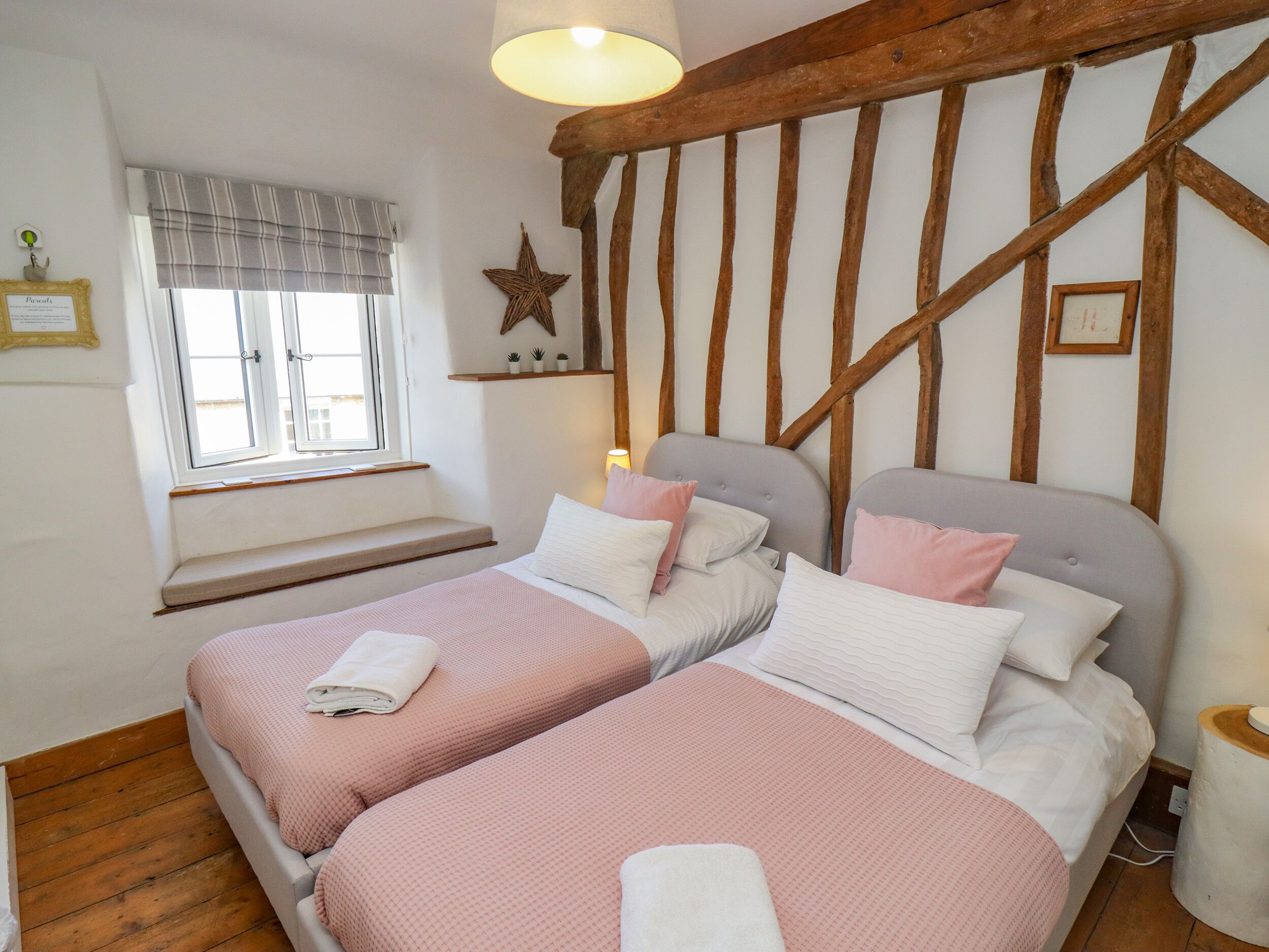 Une chambre avec deux lits, une fenêtre avec des stores, un plafond avec des poutres en bois et une décoration en forme d’étoile sur le mur.