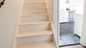 A staircase leading to a kitchen area with white cabinets and a dishwasher. - Holly Cottage (Witney)
