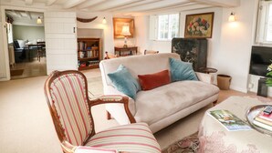 A cozy living room with a sofa, striped armchair, and a coffee table with magazines and a remote control. - Holly Cottage (Witney)