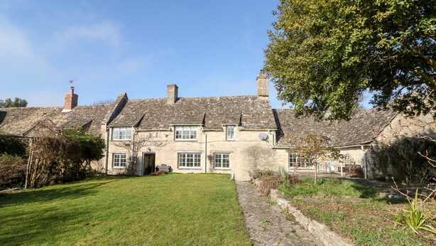 A stone house with a grassy lawn and a stone pathway leading to the entrance. - Holly Cottage (Witney)