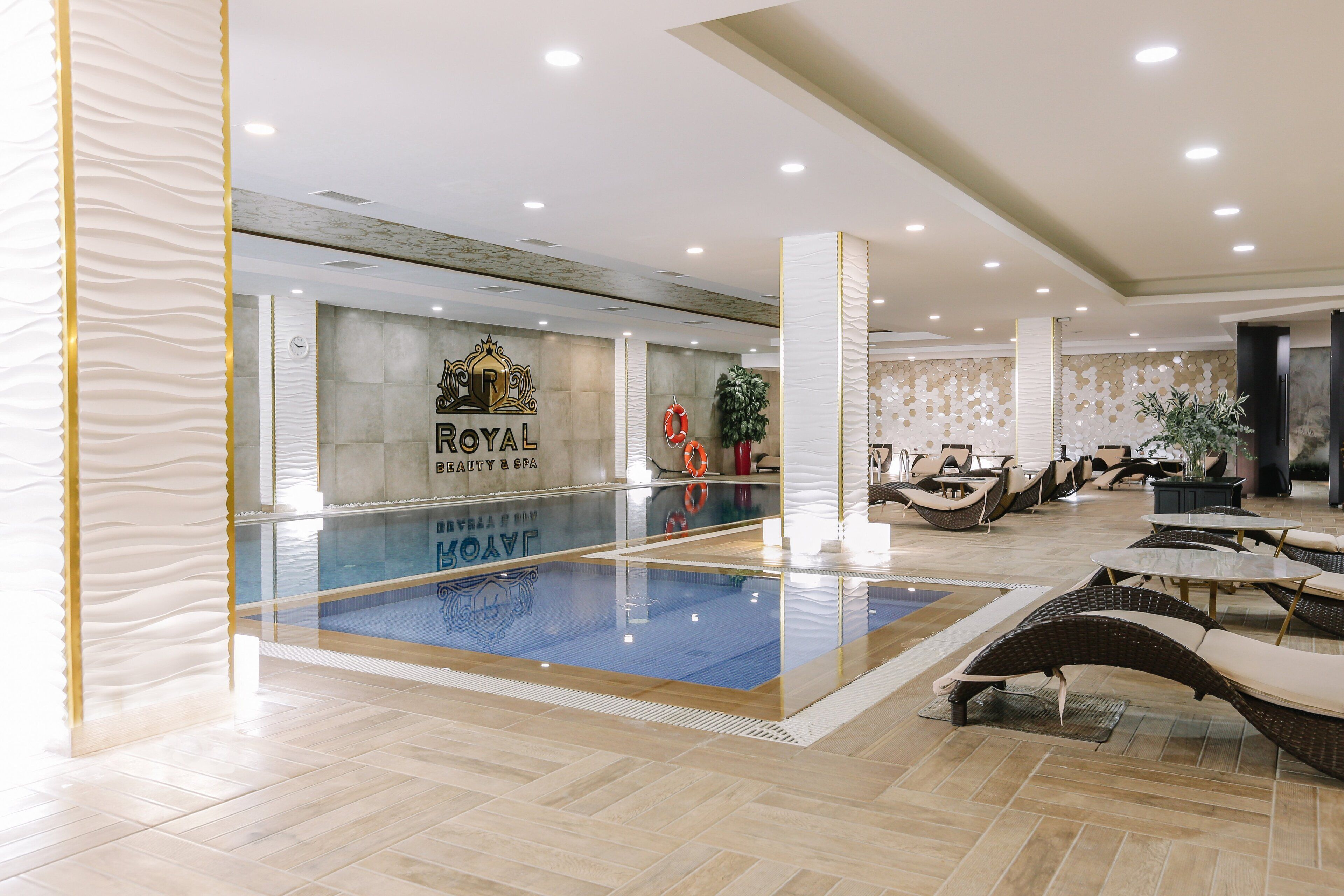 Un hall de hotel con piscina, sillones de descanso y un cartel que dice "ROYAL BEAUTY & SPA".
