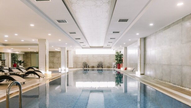 A large indoor swimming pool with lounge chairs and a seating area. - Somerset City Centre Atyrau (Atyrau)