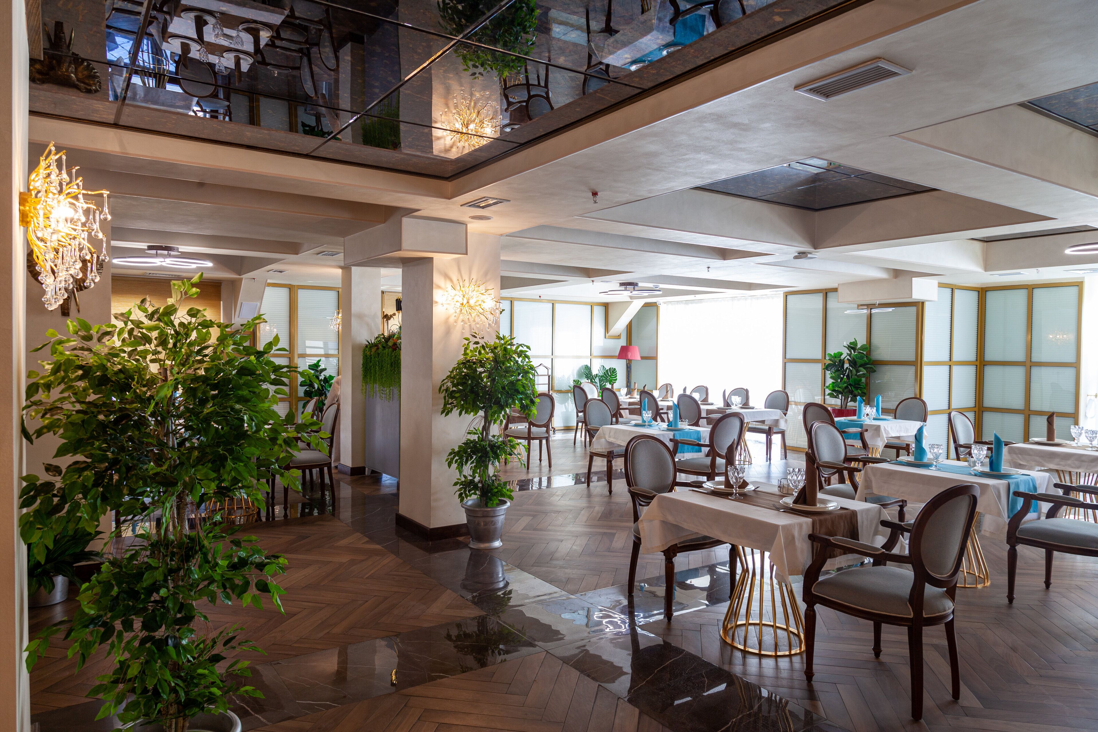 Een ruime eethoek met meerdere tafels en stoelen, potplanten en een hoog plafond met zichtbare balken.