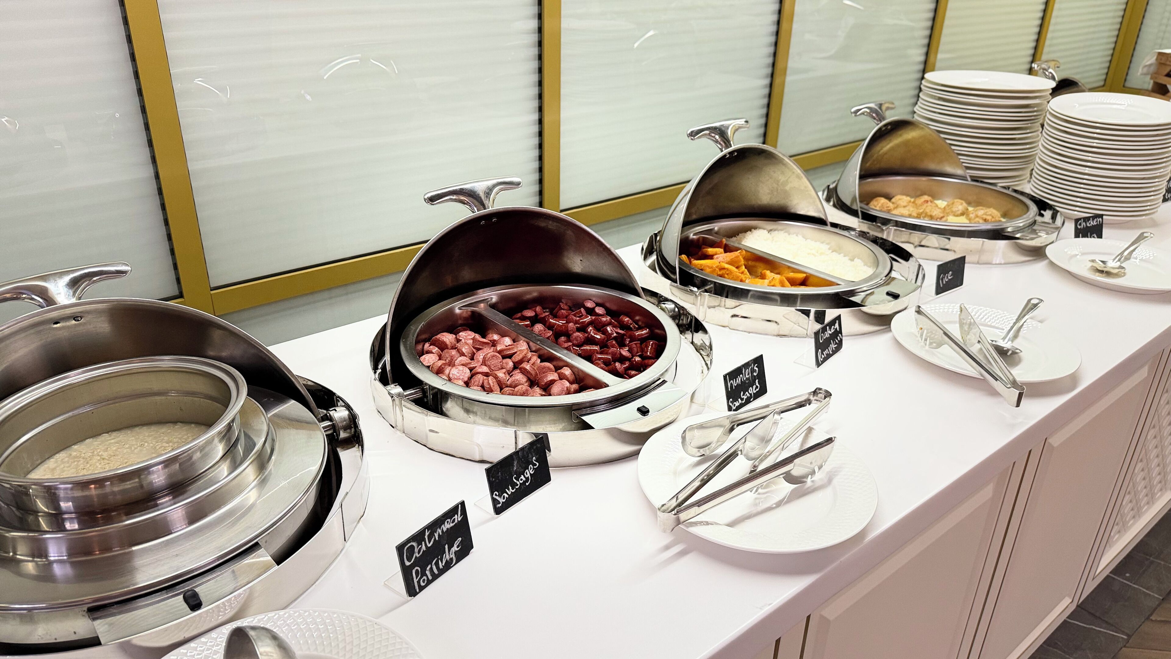 Ein Buffet mit verschiedenen Speisen, darunter Wurst, Hähnchen und Haferbrei.