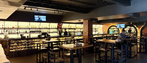 A bar area with multiple seating options, a television screen, and a variety of bottles on shelves.