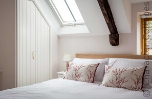 A bedroom with a skylight, a wooden headboard, and two decorative pillows. - Oyster Barn (Cheltenham)