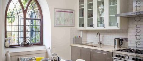 Cocina con armarios blancos, estufa a gas y ventana con una bicicleta afuera.