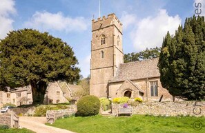 A historic stone church with a tall bell tower, surrounded by lush greenery and traditional stone buildings.