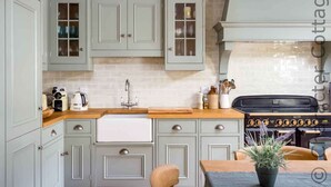 A kitchen with light grey cabinets, a white countertop, a stainless steel sink, and a black stove. - Willow Cottage (Cheltenham)