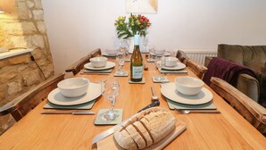 Un tavolo da pranzo in legno apparecchiato con ciotole, piatti, posate e una pagnotta di pane su un tagliere.