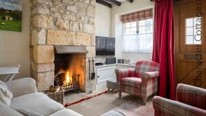 A cozy room with a stone fireplace, plaid furniture, and a television. - Lanes Cottage (Chipping Campden)