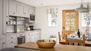 Una cocina con armarios blancos, un microondas y una zona de comedor con una mesa y sillas de madera.