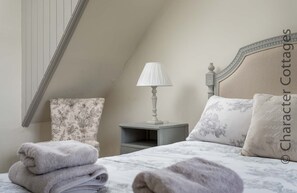 Un dormitorio con una cama, una mesita de noche, una lámpara y un almohadón estampado con motivos florales.