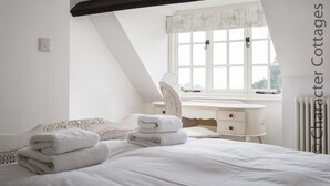Un dormitorio con cama, mesita de noche, espejo y ventana con cortinas.