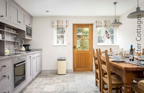 Una cocina con armarios grises, una puerta de madera y un comedor con mesa lista para cuatro.