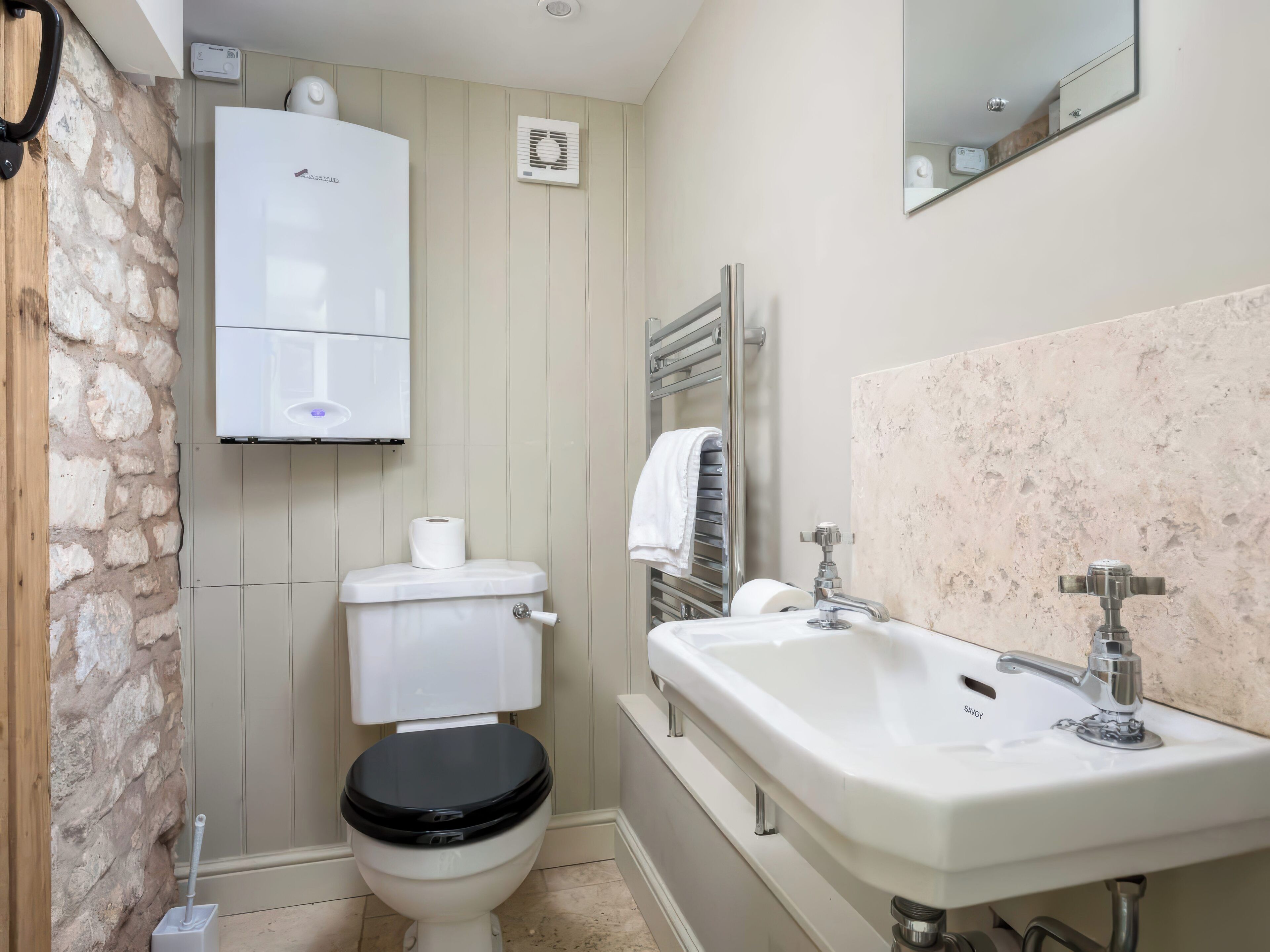 Un baño con inodoro, lavamanos blanco, espejo y perchero para toallas.
