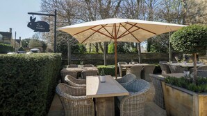 Terrassenmöbel aus Rattan mit Tisch und Stühlen, ein großer Sonnenschirm und ein Schild mit der Aufschrift 'The Wild Rabbit'.