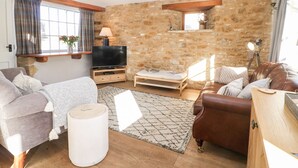 Ein gemütliches Wohnzimmer mit Steinwand, Flachbildfernseher, Sofa, Couchtisch und einer Lampe.