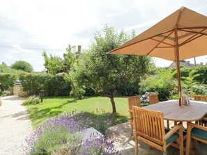 Un patio con una mesa y sillas, rodeado por un jardín de lavanda y árboles.
