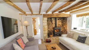 Un salon chaleureux avec une cheminée en pierre, des poutres en bois et deux canapés garnis de coussins.