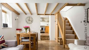 Un salon chaleureux avec un coin repas, un escalier et une cuisine en arrière-plan.