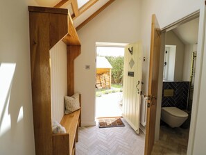 Un banco de madera con un cojín, una puerta que da a un jardín y un baño con inodoro y toallero.