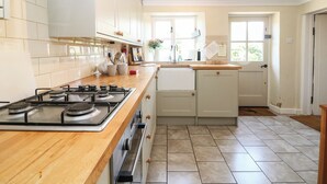 A modern kitchen with white cabinets, a wooden countertop, a gas stove, and a built-in oven. - Primrose Cottage (Cheltenham)
