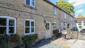 A stone building with multiple windows, a door, and a small outdoor seating area with tables and chairs. - Primrose Cottage (Cheltenham)